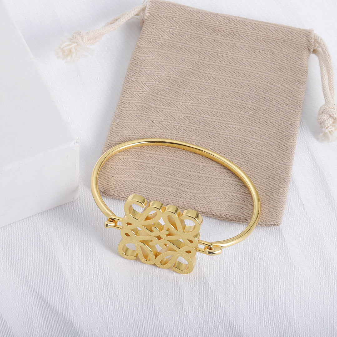 Gold open cuff bracelet with cutout logo centerpiece, shown on a beige pouch
