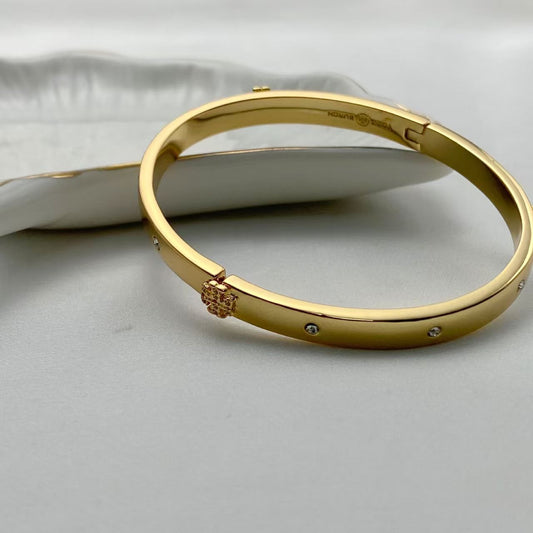Gold hinged bangle with Pace logo charm and clear crystal accents