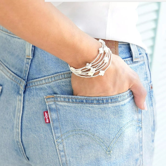 Layered silver-tone beaded cross bracelets with small white cross charms on wrist
