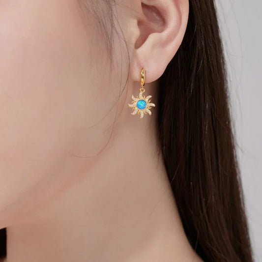 Gold hoop earrings with dangling sun charm and blue round center stone