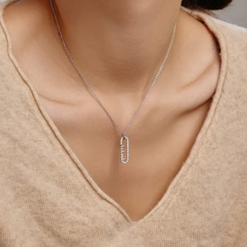 Silver paper clip pendant necklace on neckline, V-neck sweater fabric visible.