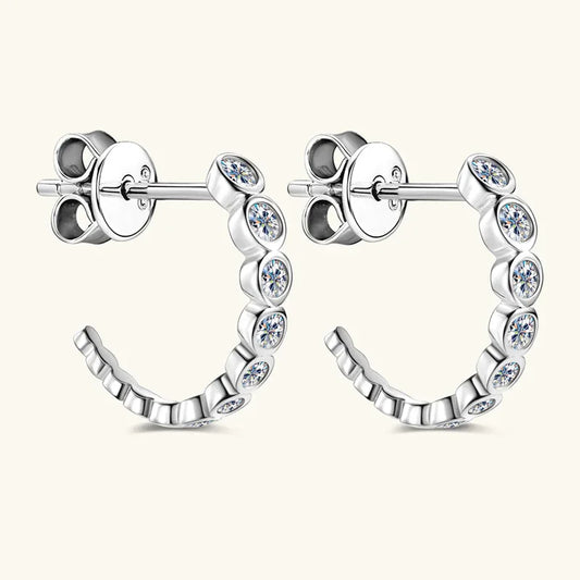 White gold C-hoop earrings with bezel-set round moissanite stones and hinge clasp.