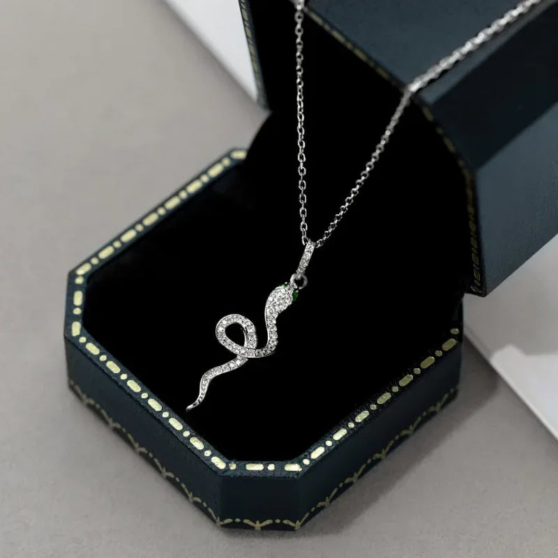 Silver snake pendant necklace with green CZ accents, shown on display box