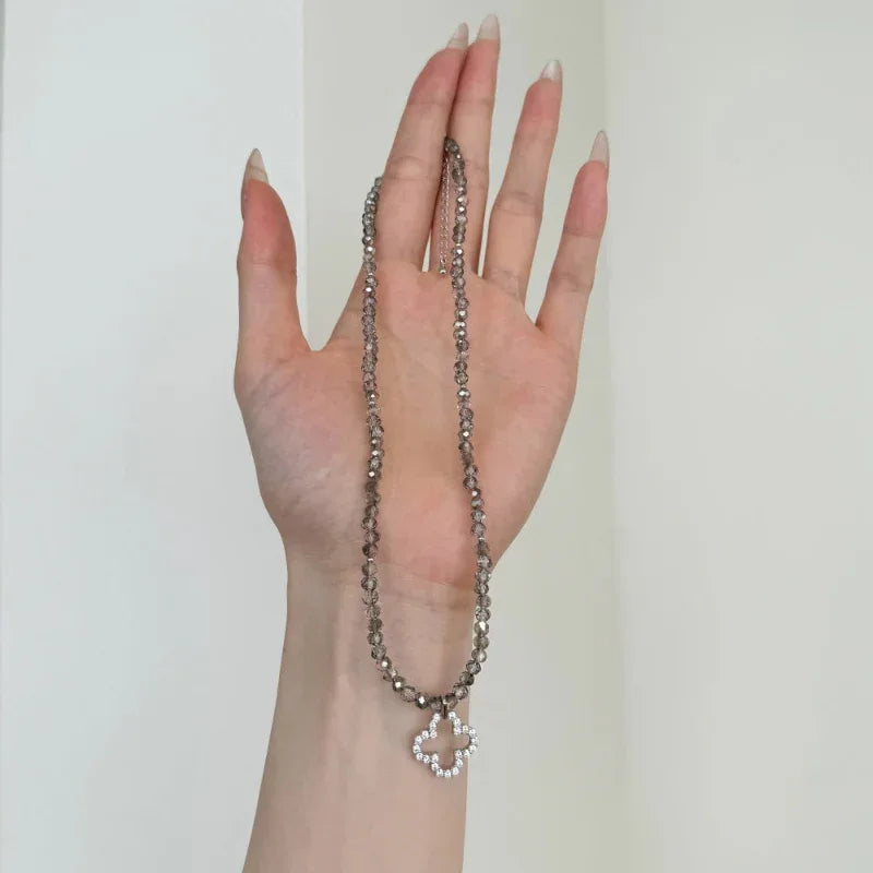 Silver crystal chain necklace with four-leaf clover charm resting on palm