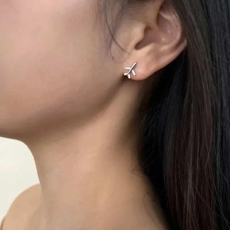 Mini airplane stud earrings, silver-toned with clear stones, close-up on ear.