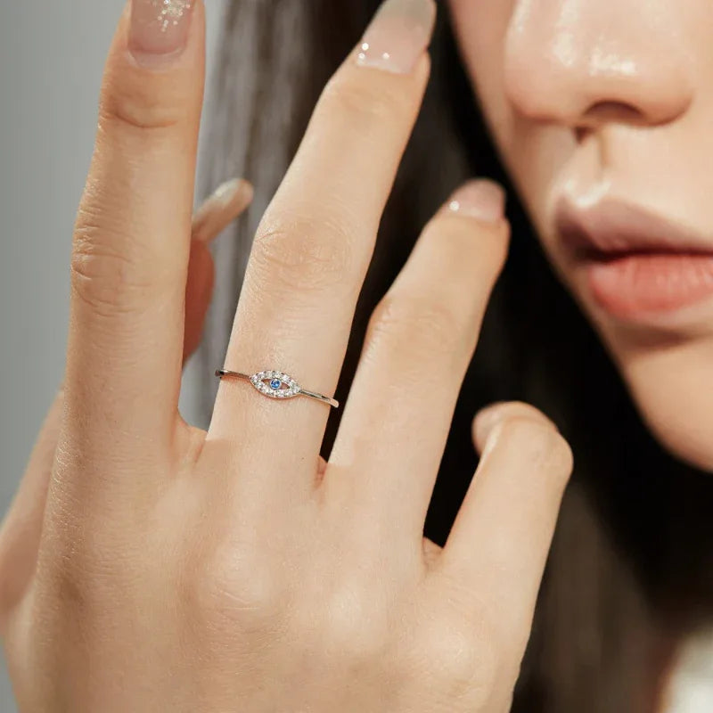 Silver ring on hand with blue eye CZ center and clear halo, thin band