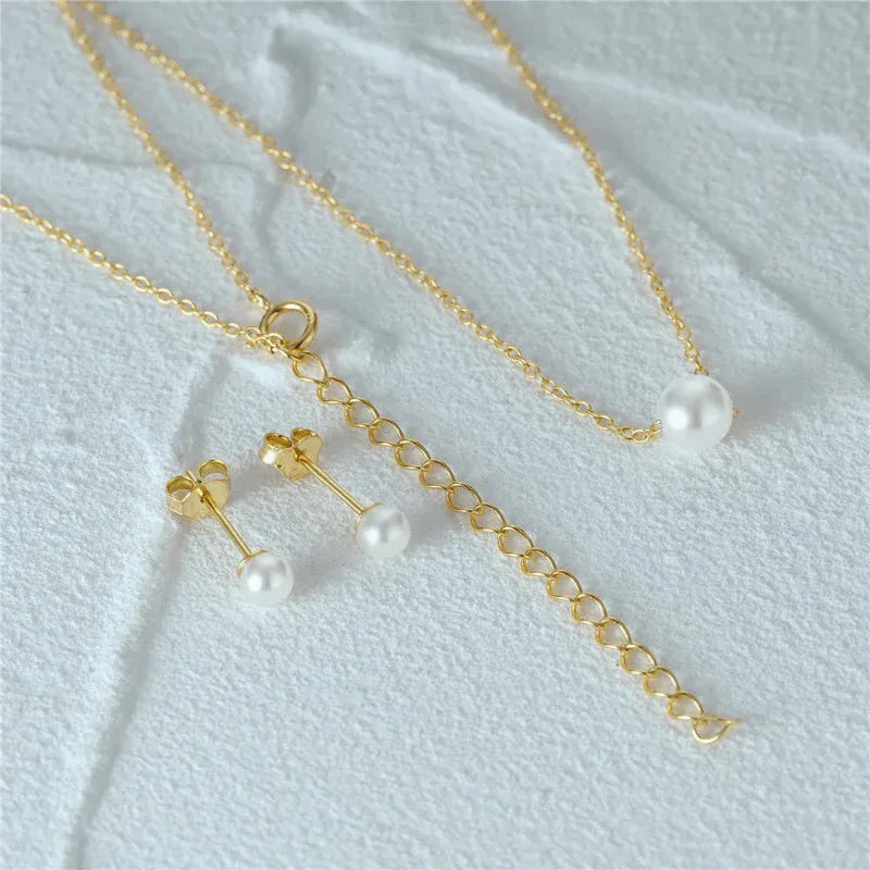 Gold pearl jewelry set closeup: chain necklace, pearl stud earrings, and bracelet chain.