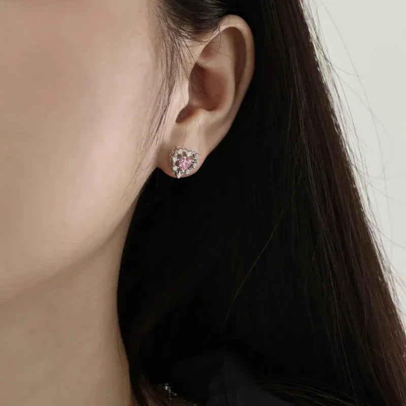 Heart-shaped stud earrings with pink heart gemstone and clear pavé detail, profile view.