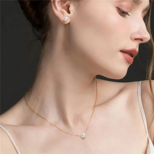 Gold pearl jewelry set on model: pendant necklace and pearl stud earrings.