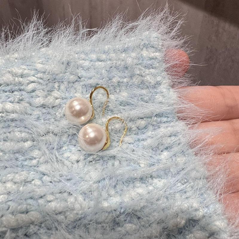 Round pearl hook earrings with gold-tone hooks and two white round pearls on soft fabric