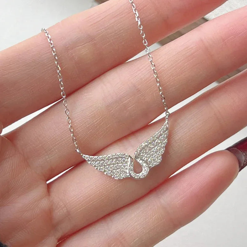 Silver angel wing pendant necklace with CZ stones, chain held in hand