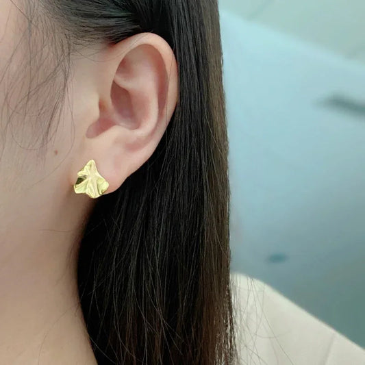 Gold-tone abstract stud earrings on a model's ear with slim post backs.