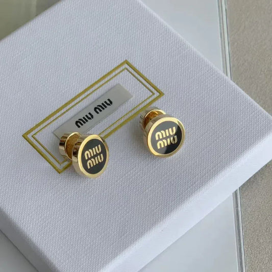 Round enamel stud earrings on white box, black 'miu miu' discs with gold tone