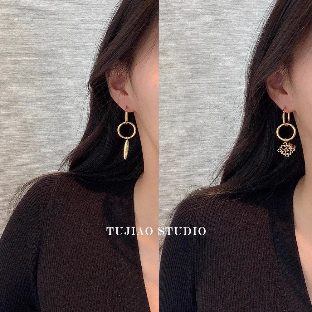 Gold asymmetrical hoop earrings with dangling charm worn by a model