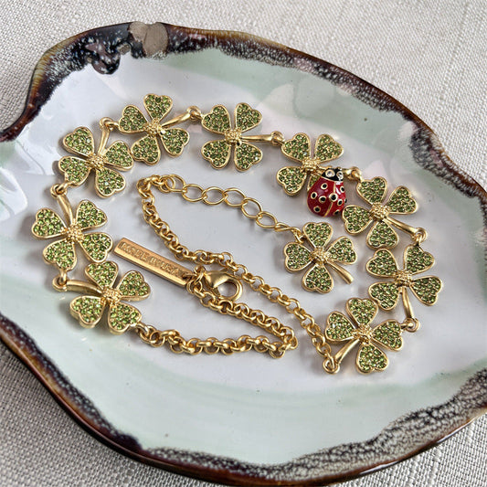 Gold-tone clover crystal necklace with ladybug bead, shown on jewelry dish