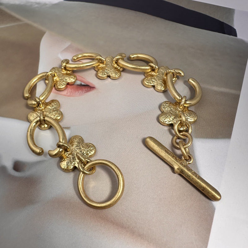 Gold-tone bracelet with floral charms, open-link chain, and long bar toggle clasp