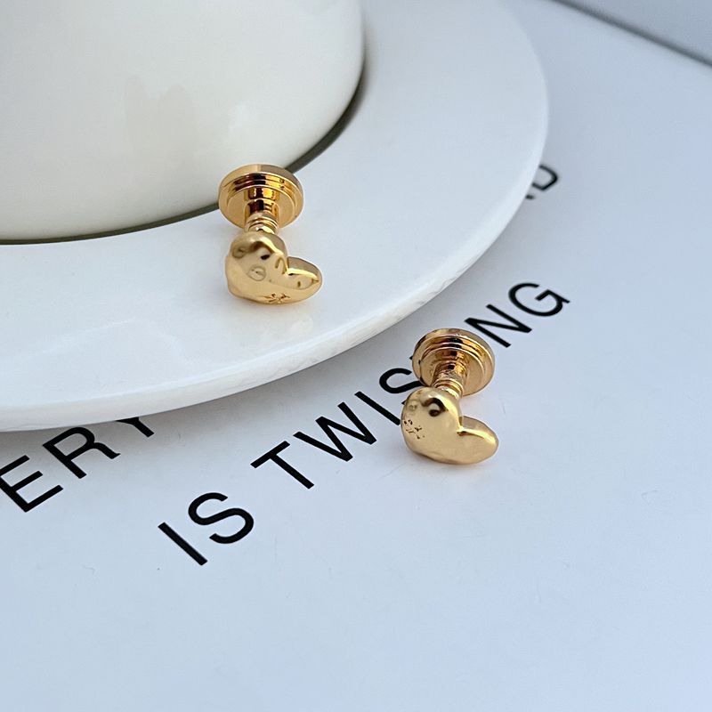 Gold heart-shaped earrings with stud posts, close-up on one heart back