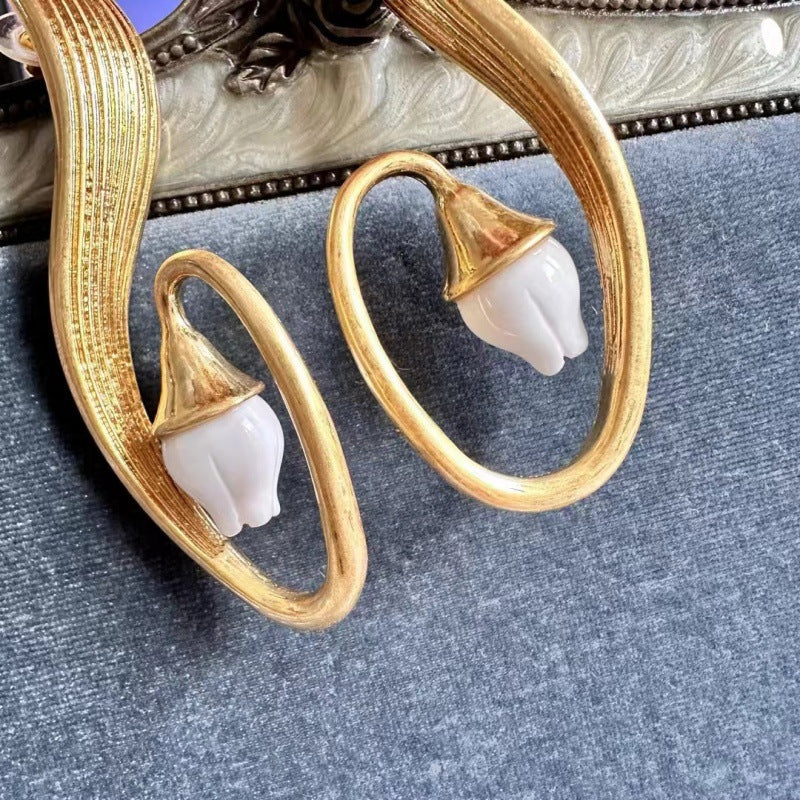 Close-up gold clip-on earrings with white flower petal detail on crescent hoops