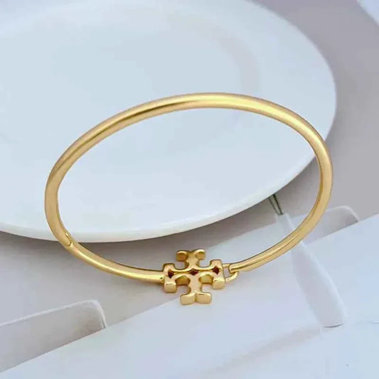Gold open metal bangle with centered logo emblem detail