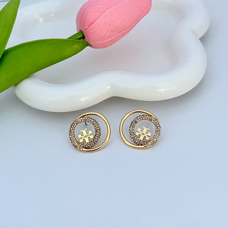 Gold-tone rhinestone halo stud earrings, circular logo center with polished gold rim