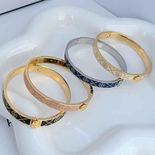 Two open enamel metal bracelets with gold-tone bands, one dark patterned and one blue patterned
