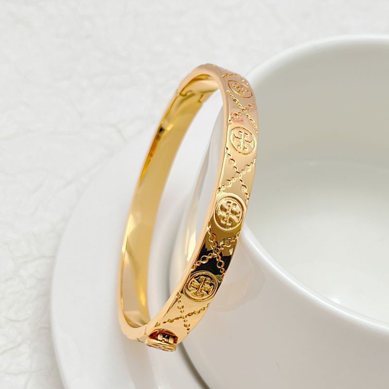 Gold cuff bangle view from side, featuring logo engraving and red gem at hinge