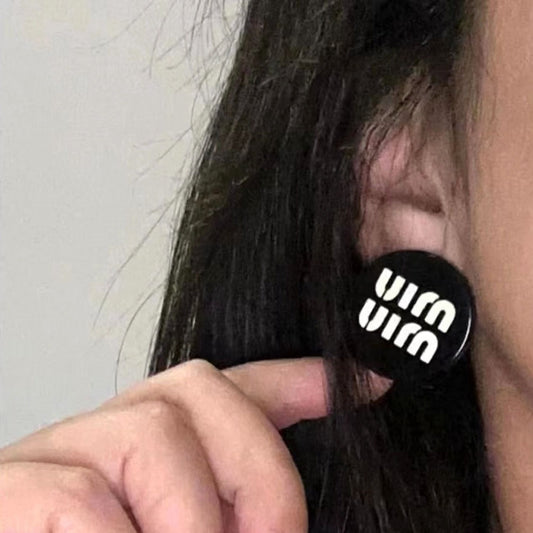 Black round resin button stud earrings with logo, worn on ear.