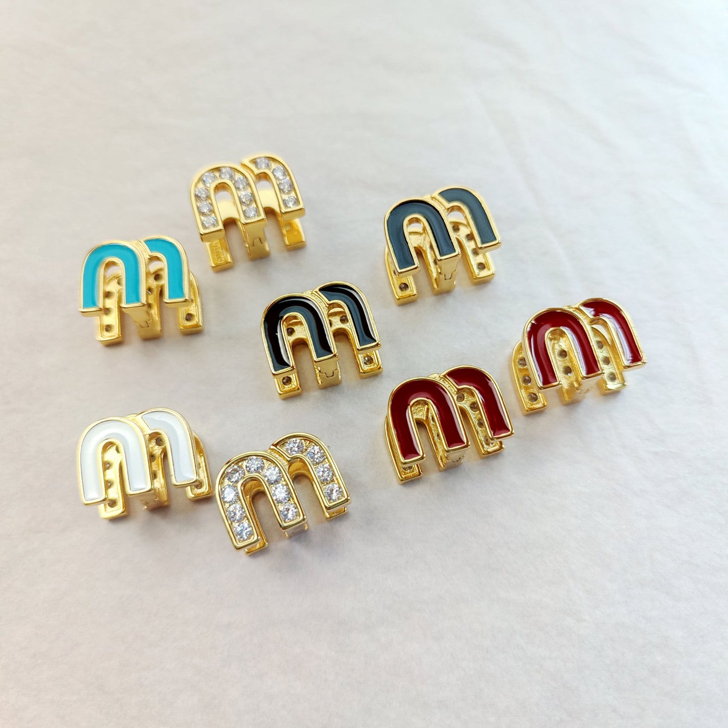 Set of enamel M stud earrings with blue, black, red, and white enamel and crystals