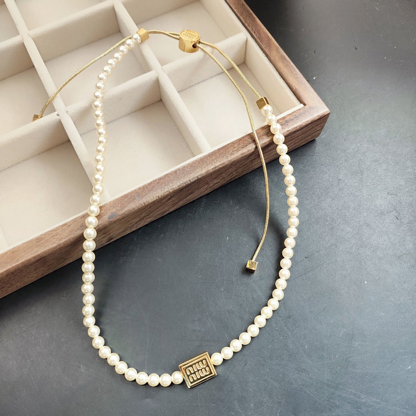 Pearl necklace with gold tone tag charm and adjustable cord, clasp detail shown