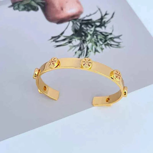 Gold open bangle cuff with embossed lion-like medallions and red stud accents