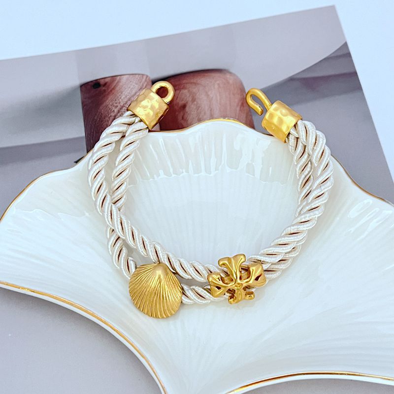 White braided cord bracelet with gold toggle clasp and shell logo centerpiece