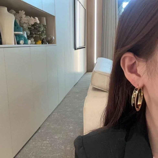 Gold-tone hoop earrings with black and white enamel insert, worn on ear