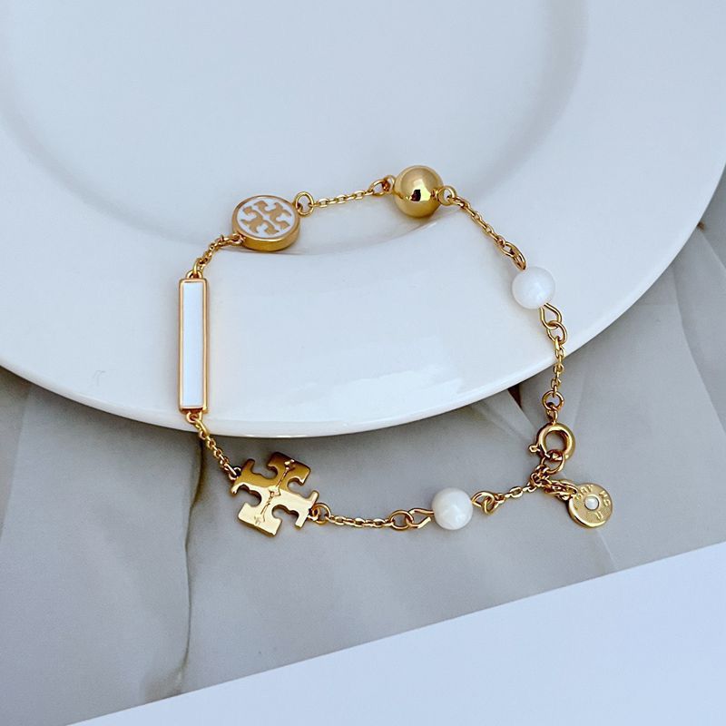 Gold-tone logo charm bracelet with white round beads, enamel puzzle charm, and vertical bar