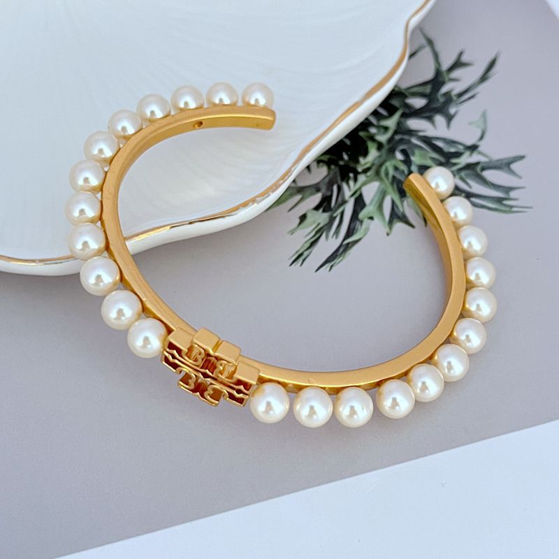 Gold open bangle with white pearl trim and red enamel logo front