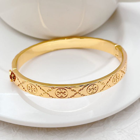 Gold bangle bracelet with circular logo medallion engraving along the band