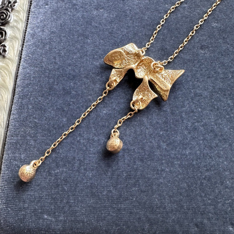 Gold-tone bow pendant necklace with round crystal drops and chain tassels