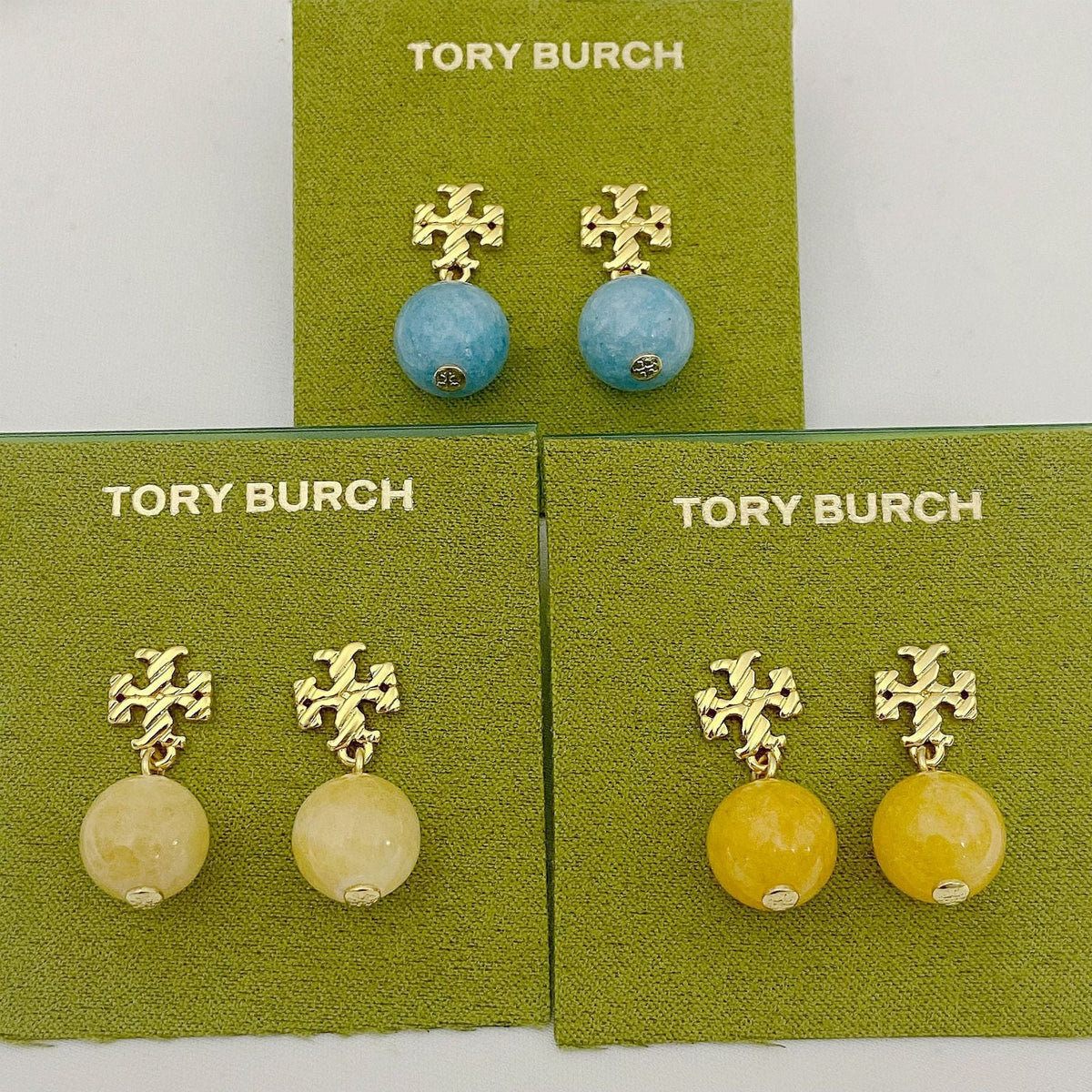 Gold-tone logo charm agate ball earrings on display cards (blue, off-white, yellow)