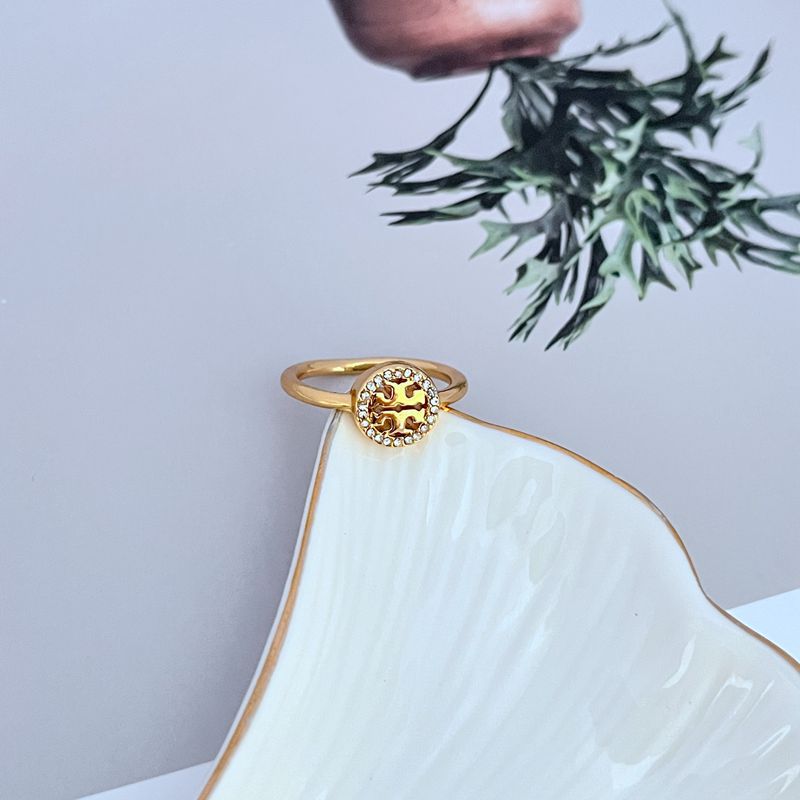 Gold-tone ring top view: round logo medallion with pavé edge stones