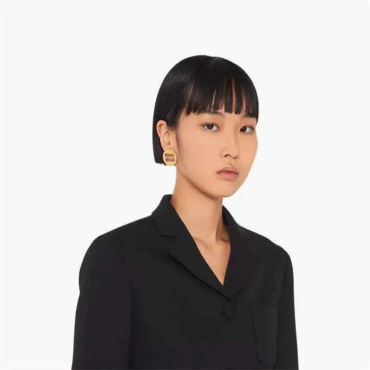 Round stud earrings on model, gold-tone discs with hollow "miu miu" logo
