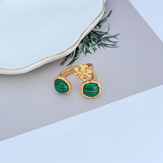 Gold-tone open metal ring with acrylic logo and green stone accents