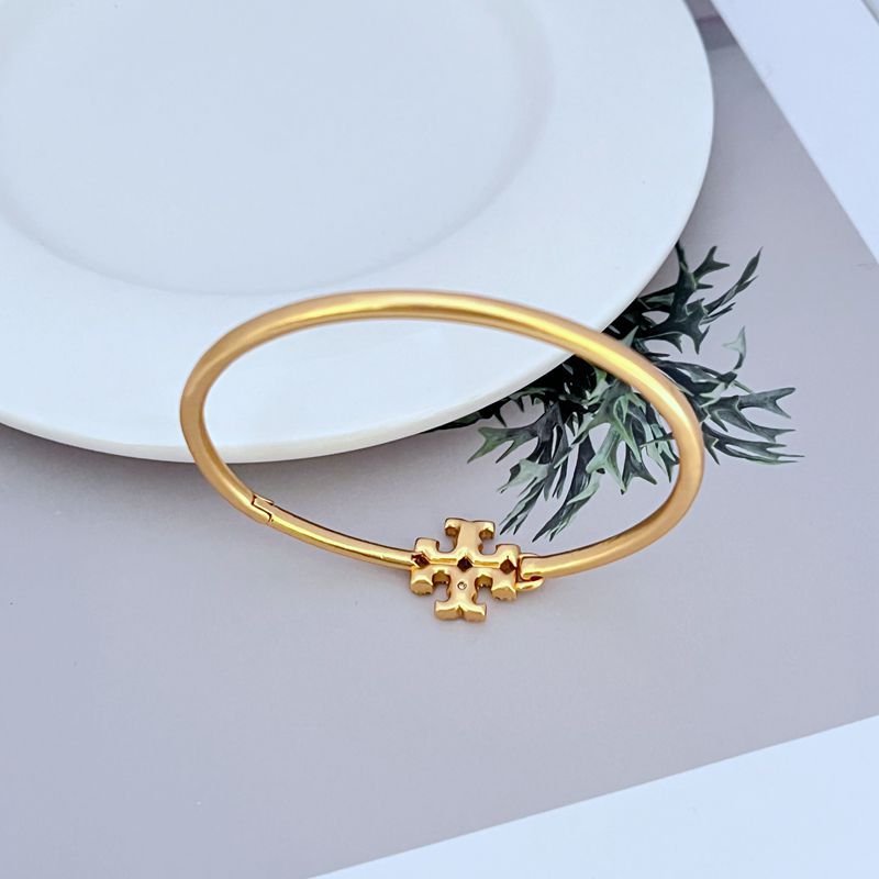 Gold-toned openable bangle with enameled diamond cross charm at center
