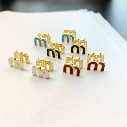Assorted enamel M stud earrings: blue, white, black, and red with gold-tone details