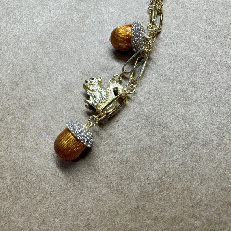 Gold-tone squirrel and acorn charm necklace with rhinestone-set segments and orange beads.