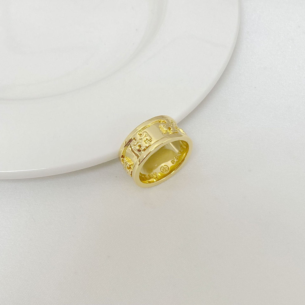 Gold metal letter band ring, close-up view with engraved vertical details