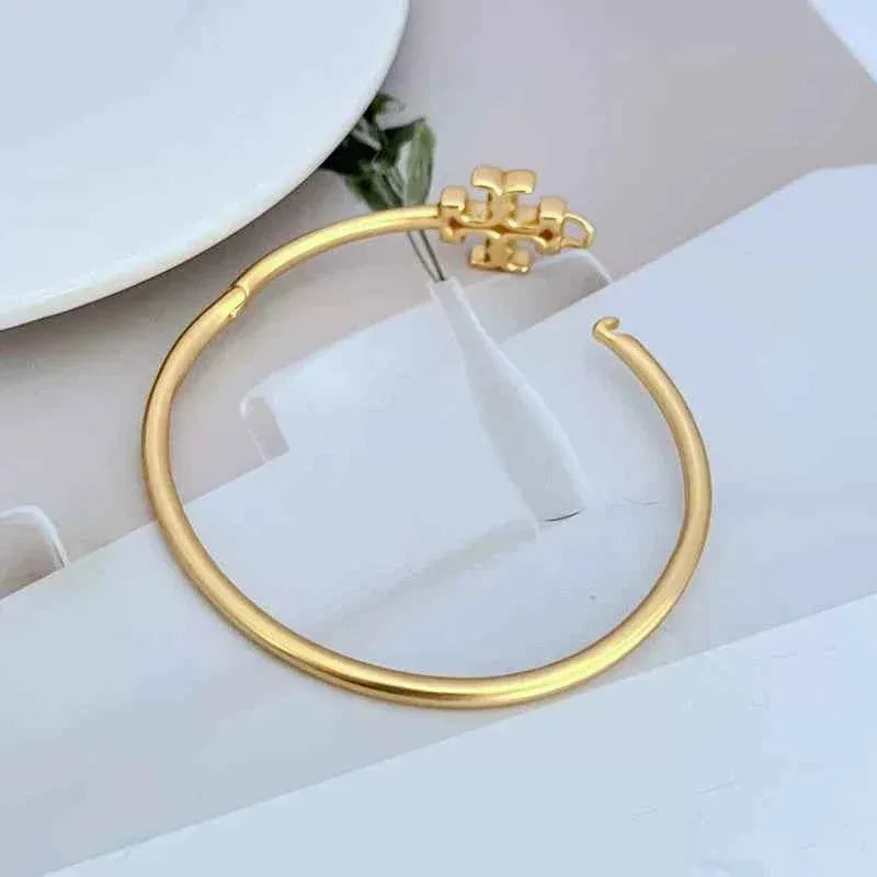Gold open metal bangle with logo emblem at top edge
