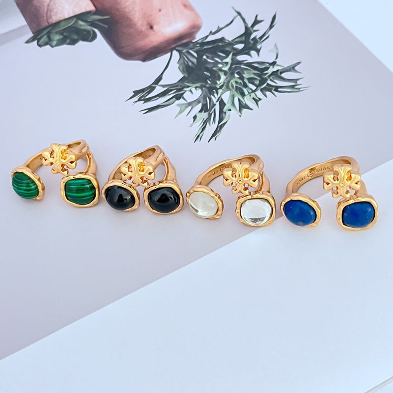 Gold-tone open metal ring with acrylic logo details and mixed colored stones