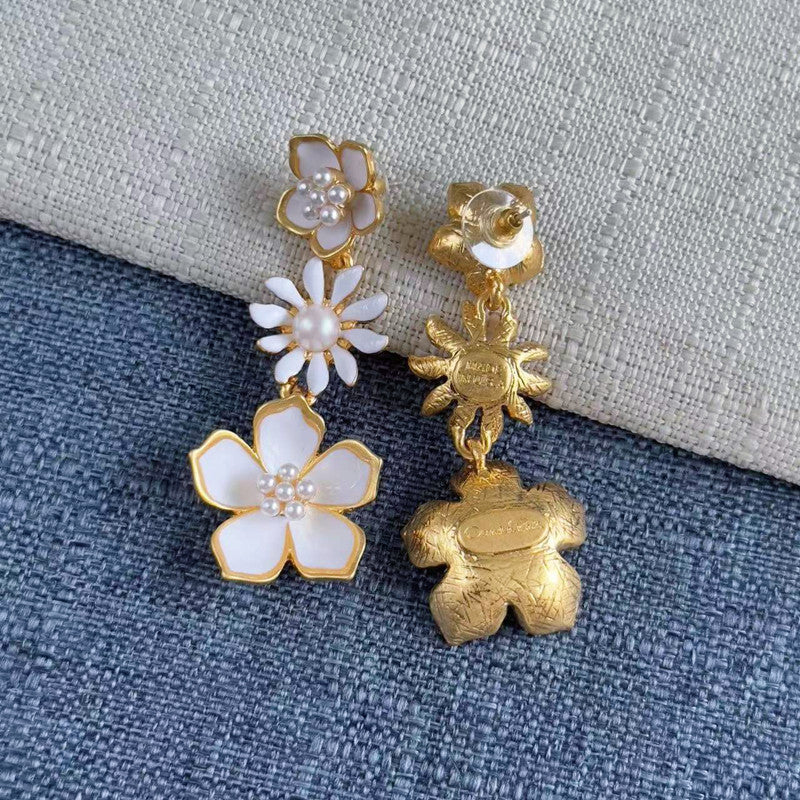 Gold drop earrings with white enamel flowers and pearl accents, shown from back