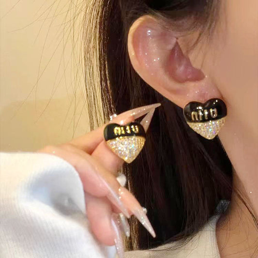 Black enamel heart stud earrings with gold-tone logo and sparkling rhinestone pavé