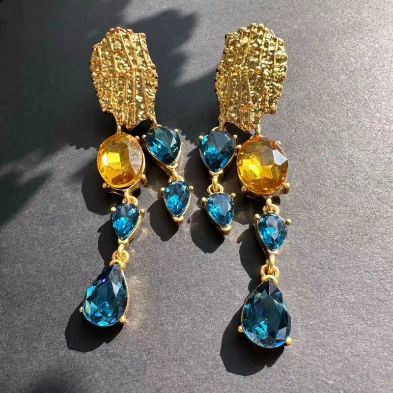 Crystal tassel earrings with gold textured studs and blue teardrop gems with amber and green accents
