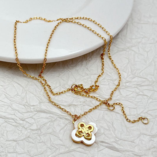 Gold-tone pendant necklace with white inlaid four-leaf clover charm and layered links